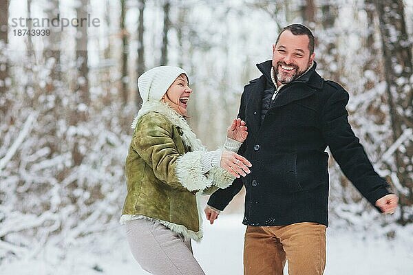Lovely glücklich mittleren Alters Familie Paar Spaß im Freien in der Wintersaison Urlaub zusammen  wobei Spaziergang durch verschneite Wald mit Lächeln  in warme Kleidung gekleidet. Liebe und Freizeit Konzept