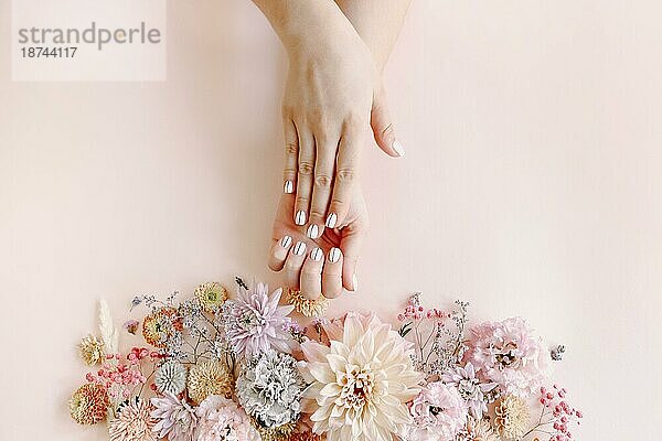 Draufsicht auf Ernte unerkennbar weiblich mit blühenden Blumen demonstrieren stilvolle saubere Maniküre auf rosa Hintergrund