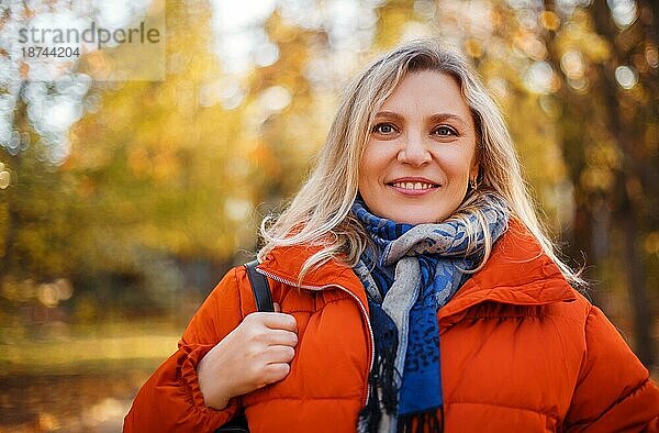 Zufriedene Frau in Oberbekleidung lächelnd an einem sonnigen Wochenendtag im Herbstpark