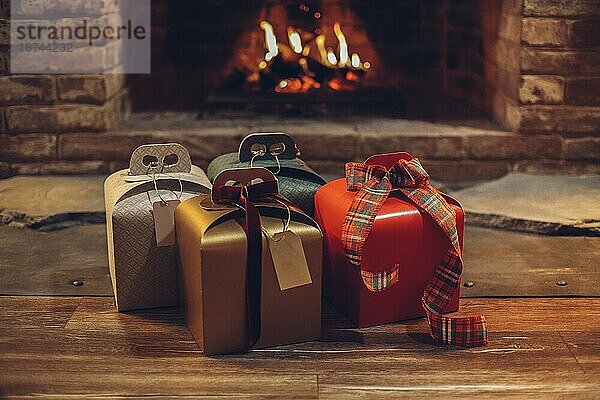 Frohe Weihnachten und ein gutes neues Jahr. Vier Weihnachtsgeschenke auf Holzboden in der Nähe von brennenden Kamin  niemand. Stapel von verpackten Weihnachtsgeschenken. Selektiver Fokus