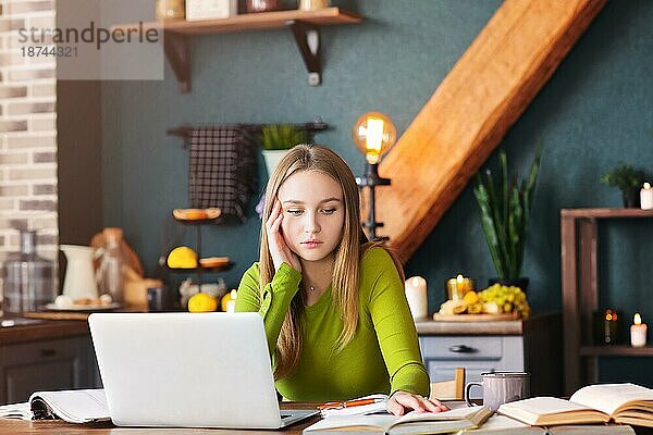 Junge nachdenkliche Frau Freiberufler sitzt am Tisch zu Hause mit Laptop  macht Notizen  starrt nachdenklich in die Luft  denkt über neue Ideen  weibliche Bloggerin auf der Suche nach Inspiration. Freiberufliches Konzept