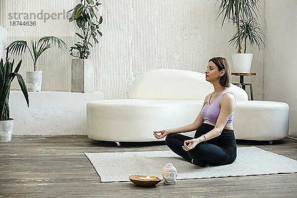 Schöne schwangere Frau sitzt in Yoga Position im Spa Raum  hält coco Kerze  entspannen und meditieren  während das Tragen sportlichen Outfit  zeigt nackten Bauch. Gesundheit Lifestyle Schwangerschaft Schönheit  Interieur