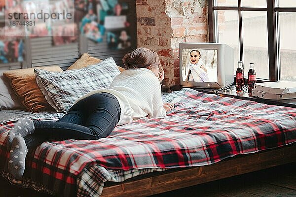 Unerkennbare Frau  die sich auf einem bequemen Bett mit karierter Decke ausruht und zu Hause Retro TV schaut