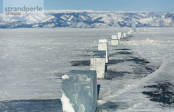 Eiswürfel auf dem idealen glatten Eis des Baikalsees mit Eishügeln am Horizont. Die Sonne scheint durch die Seiten der Eiswürfel. Die Schollen sehen aus wie Diamanten