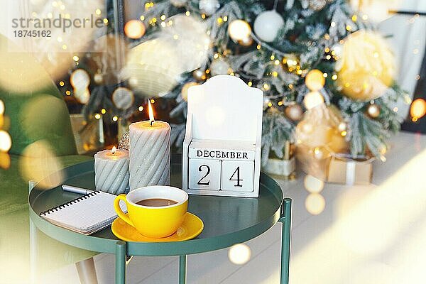 Heiligabend Datum. 24. Dezember auf hölzernen Kalender stehen auf kleinen Tisch mit brennenden Kerzen im Wohnzimmer  selektiven Fokus. Weihnachten und Neujahr Konzept