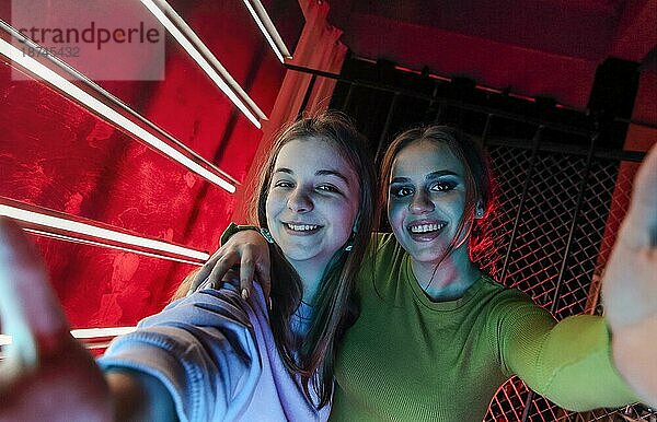 Selfie Porträt von zwei glücklichen besten Freundinnen  junge Mädchen mit natürlichem Make up in stilvoller Kleidung  die sich gegenseitig an den Schultern umarmen  Spaß auf einer Disco Party haben und mit strahlendem Lächeln in die Kamera posieren