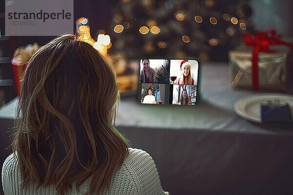 Glückliche junge Frau  die einen Cocktail trinkt und sich mit Freunden über einen virtuellen Zoom Videoanruf unterhält  um eine Neujahrsparty in einem Online Konferenz Chat auf einem Computer zu Hause zu feiern