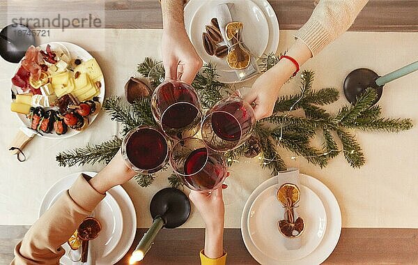 Draufsicht auf anonyme Freunde  die am weihnachtlich geschmückten Tisch mit einem Glas Wein anstoßen