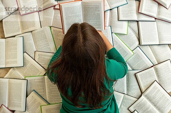 Draufsicht auf eine anonyme Studentin  die während der Prüfungsvorbereitung auf Büchern liegt und liest