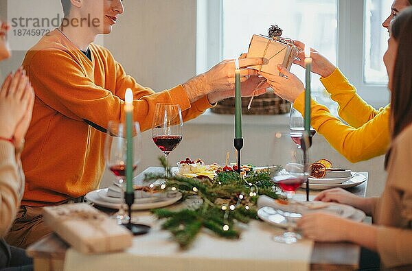 Glückliche Person  die einem Freund ein eingepacktes Geschenk gibt  während sie am Tisch sitzt und gemeinsam Weihnachten feiert