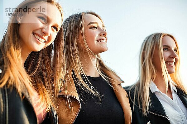 Glückliche junge Frauen  die an einem sonnigen Wochenendtag auf einer Straße in der Stadt auf dem Bürgersteig gehen und lächeln