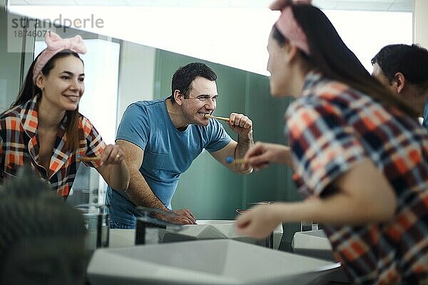 Glückliches junges brünettes Paar beim Zähneputzen im Badezimmer  liebevoller Mann und seine Frau  gemeinsame Morgenhygiene  Bindung zu Hause  selektiver Fokus auf Spiegelreflexion