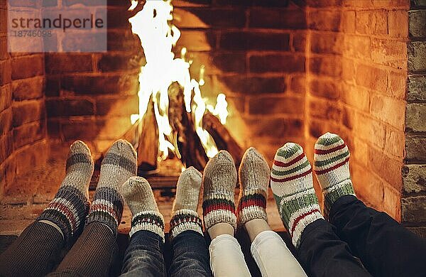 Familie in warmen Wollsocken ruht am Kamin zu Hause zur Weihnachtszeit  Ausschnitt. Mutter  Vater und zwei Kinder wärmen die Füße am Feuer  während sie die Winterferien zusammen in gemütlicher Atmosphäre verbringen