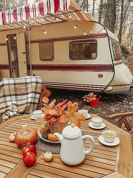 Holzstühle und Tisch mit Teeset vor gemütlichen Retro Wohnwagen auf Herbst Tag in friedlichen Landschaft platziert