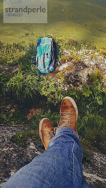 Wanderrucksack und Beine in Sportschuhen einer jungen Frau  die sich bei einer Bergwanderung im Tal ausruht  aktiver gesunder Lebensstil im Freien Erholung