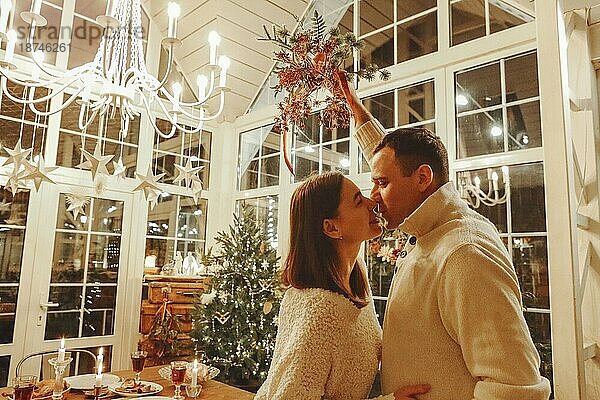 Mitternachtskuss. Junge glückliche Familie Paar in der Liebe küssen und umarmen während Silvesterfeier in gemütlichen festlich geschmückten Raum mit Weihnachtsbaum und festlichen Esstisch