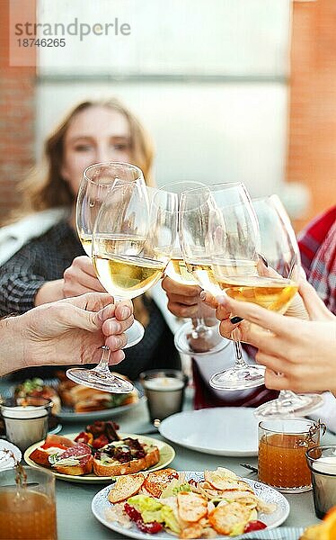 Eine Gruppe anonymer Personen stößt während einer Party auf dem Dach mit Weingläsern an und bringt einen Toast aus