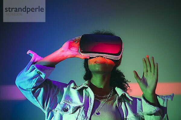 Virtuelle Realität. Junge afroamerikanische Frau mit VR Headset Brille  die mit dem Cyberspace interagiert und die virtuelle Welt unter Neonlicht erkundet  gestikuliert mit der Hand. Digitale Spiele und Unterhaltung