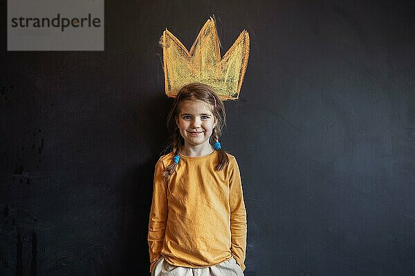 Niedliches kleines Mädchen mit zwei Zöpfen hat Spaß Kreidezeichnung der Krone auf dunklem Hintergrund durch ihren Kopf