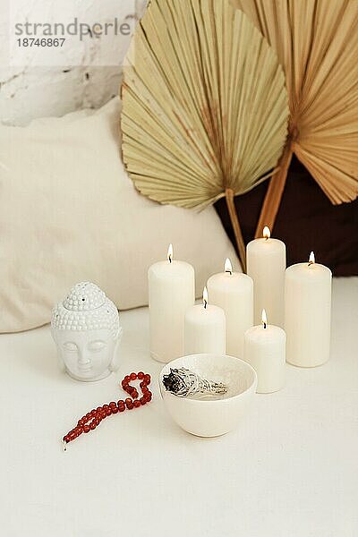 Meditationsplatz mit brennenden Kerzen und weißem Salbei Räucherstäbchen  aus dem Rauch aufsteigt  kleine Statue eines Buddhakopfes  Aromatherapie mit Reinigung von negativer Energie  Vertikalaufnahme