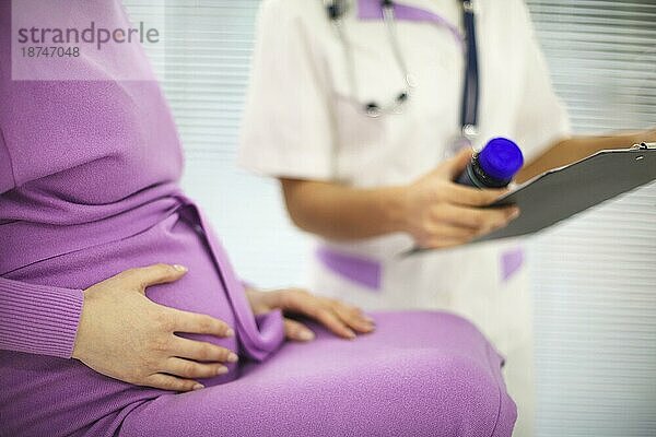 Schöne junge Mixed race Ärztin mit schwangerer Patientin vor Teilnehmerin  Pillenglashalter und geschriebenes Rezept auf Formular. Medizin und Apotheke Konzept. Gesundheitswesen Konzept