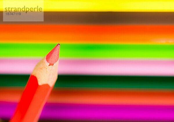 Spitze eines roten Holzbleistifts mit farbigen Buntstiften im Hintergrund selektiver Fokus