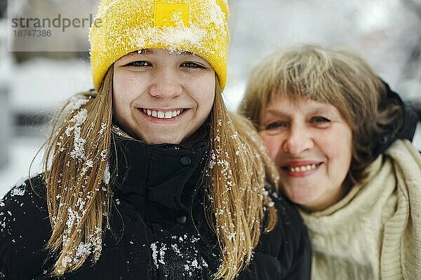 Lovely Porträt der glücklichen fröhliche Familie Großmutter und Enkelin in warmer Kleidung lächelnd glücklich in die Kamera  während Zeit im Freien im Winter auf kalten frostigen schneereichen Wetter. Selektiver Fokus