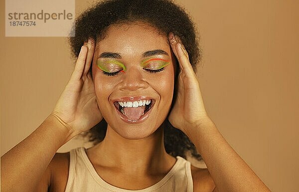 Schönheit Mode Porträt der attraktiven jungen afrikanischen amerikanischen Frau  schöne Glamour Modell mit stilvollen Neon Farbe Make up mit hellen Lächeln isoliert über beige Studio Hintergrund