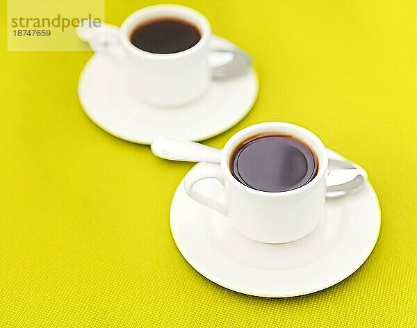 Draufsicht auf Tassen mit frischem Espresso und Löffel auf Untertassen auf gelbem Hintergrund