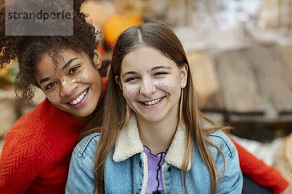 Porträt von zwei glücklichen multirassischen Freundinnen  die in die Kamera lächeln  während sie Zeit in der herbstlichen Natur verbringen  fröhliche Teenagermädchen verschiedener Rassen  die einen gemeinsamen Spaziergang im Herbstwald genießen Weibliche Freundschaft