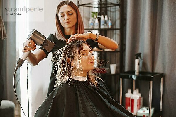 Glückliche Frau mit Friseurin beim Frisieren im Salon. Kompetente Friseurin entscheidet  was im Friseursalon mit brünetter Kundin zu tun ist. Zwei schöne Damen diskutieren über neue Frisur. Professionelle Frisur und Stylist Arbeit Konzept