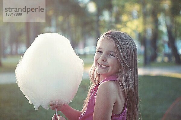 Glückliches kleines Mädchen mit süßer Zuckerwatte im Sommerpark