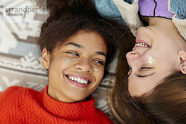 Weibliche Freundschaft. Zwei junge verschiedene Freundinnen afrikanischer amerikanischer und kaukasischer Ethnizität schauen sich mit Liebe an  während sie sich auf einem Plaid im Freien ausruhen und Spaß beim Picknick am Herbsttag haben