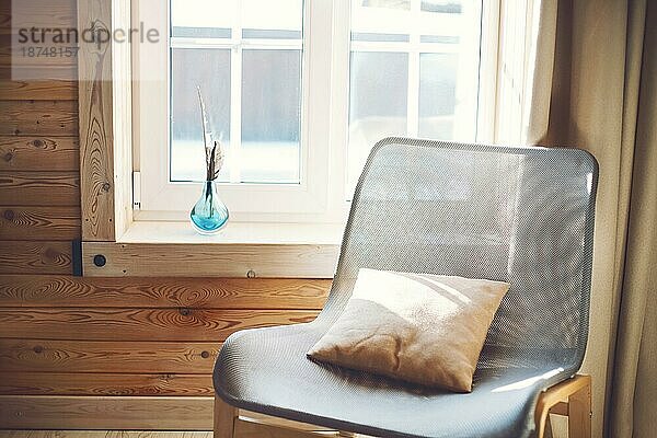 Innenraum des gemütlichen modernen Haus mit ethnischen Boho Dekoration. Sessel mit Kissen auf Holzboden  Vorhänge auf großes Fenster im rustikalen Wohnzimmer in sonnigen Tag  niemand  flach legen  freien Raum