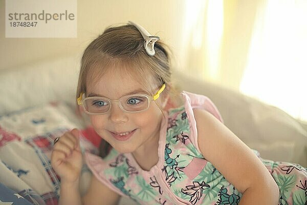 Childrens Sehkraft Konzept. Cute liebenswert kleines Mädchen mit tiefblauen Augen tragen Brille lächelnd beim Spielen zu Hause. Glückliche positive Kind mit schlechten Vision trägt eine Brille