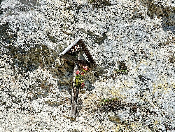 Traditionelles Holzkreuz mit Blumen an einer Felswand