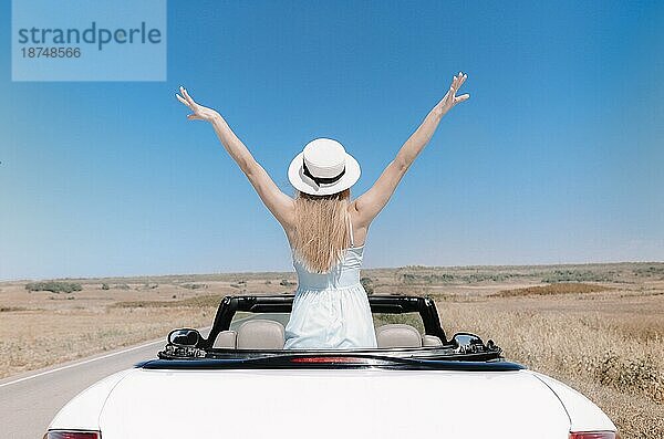 Rückenansicht einer fröhlichen jungen Frau in Sommerkleidung im Cabrio während einer Autofahrt