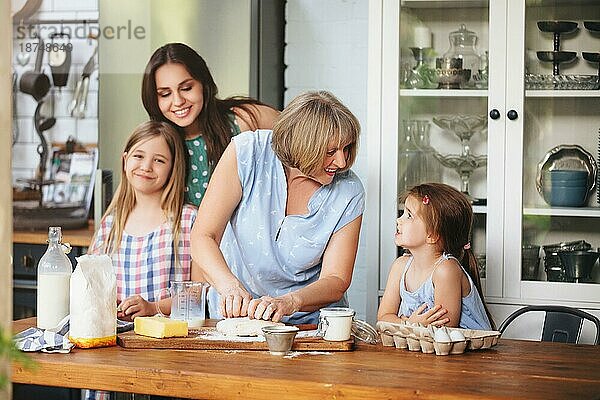 Glückliche erwachsene und reife Frauen kochen zusammen mit süßen Mädchen am Tisch in der Küche