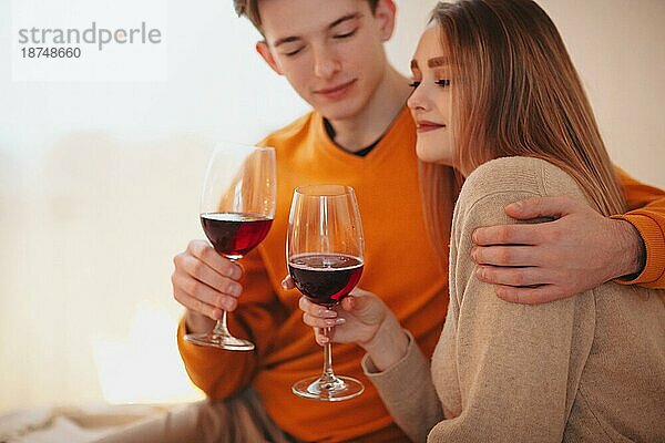 Junger Mann und Frau umarmen sich und genießen Rotwein bei einem romantischen Date zu Hause