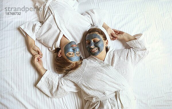 Glückliche Familie Mutter und Baby Tochter machen Gesichtsmaske  Hautpflege zusammen. Ansicht von oben