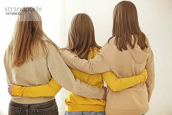 Rückenansicht von anonymen Freundinnen in Freizeitkleidung  die sich gegenseitig umarmen  vor einem beigen Hintergrund