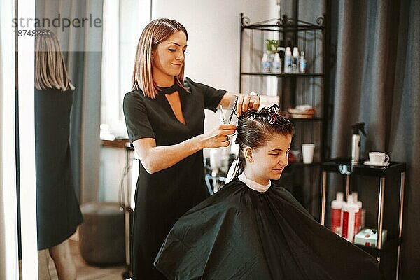 Positive Frau Friseurin bei der Arbeit Prozess in Schönheitssalon  professionelle lächelnde Friseurin Vorbereitung weiblichen Kunden für Haarschnitt  Pinning bis Haar mit Clips. Geschäft  Mode und Schönheit Konzept