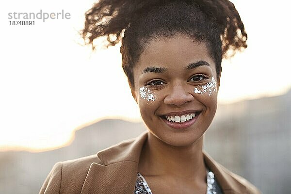 Glück Konzept. Close up Outdoorporträt von glücklichen freudigen afrikanischen amerikanischen Frau mit silbernen glänzenden Glitter auf Gesicht halten die Augen geschlossen und lächelnd glücklich während der Party oder Feier auf dem Dach