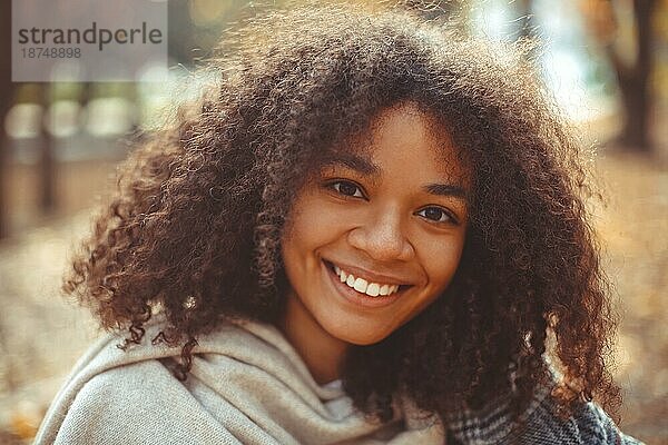 Cute Herbst Nahaufnahme Porträt der jungen lächelnd glücklich afrikanischen amerikanischen Frau mit lockigem Haar genießen Spaziergang im Park im Herbst Saison. Outdoorfoto von zufriedenen schwarzen Mädchen mit Augen in der Liebe mit dem Leben