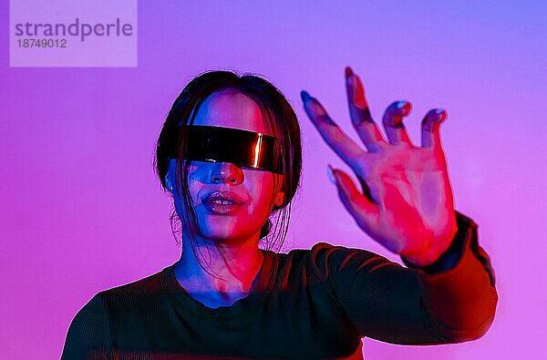 Junge Frau mit futuristischer Brille gestikuliert und schützt ihr Gesicht vor hellem Neonlicht in einem modernen Raum