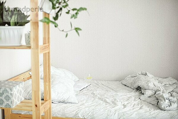Seitenansicht des morgendlichen Bettes nach dem Aufwachen mit offenem Buch und Glas Zitronenwasser darauf  zerknitterte weiße Bettlaken und Kissen. Entspannender Tag zu Hause am Wochenende Konzept