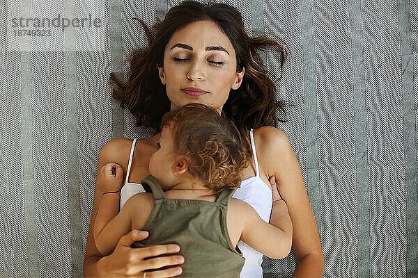 Mutterschaft Porträt. Blick von oben auf junge Frau Mutter mit niedlichen Baby an der Brust schlafen zusammen zu Hause am Tag  müde Mutter ruht auf Bett mit ihrem kleinen Sohn Kleinkind