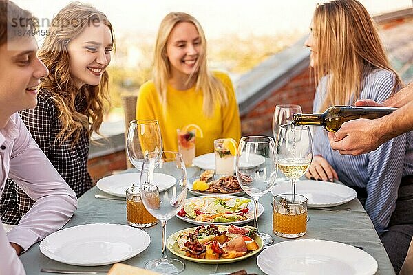 Fröhlicher Mann und lächelnde Frauen  die am Tisch sitzen und darauf warten  daß der Kellner beim Bankett den Wein in die Kelche gießt