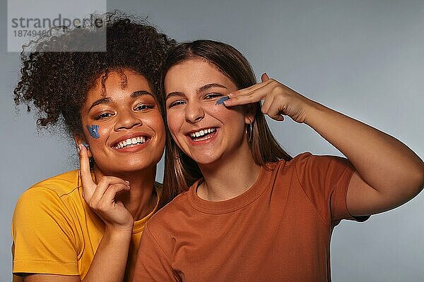 Wellness Tag. Zwei glückliche multiethnische Teenie Freundinnen  die sich beim Auftragen der Gesichtsmaske amüsieren  rassenübergreifende beste Freundinnen  die ihre Schönheitsroutine genießen und breit lächelnd in die Kamera schauen. Weibliche Freundschaft