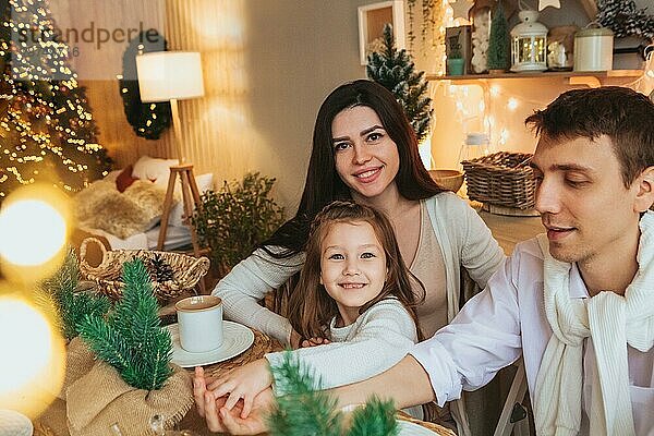 Junge glückliche europäische Familie mit Kindern genießen die Weihnachtsferien zusammen in gemütlicher Atmosphäre zu Hause. Eltern und zwei kleine Kinder Geschwister sitzen am Café Tisch und trinken Kakao mit Marshmallow